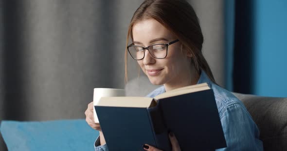 Beutiful Girl Reading Book and Drinking Coffee on Couch alt
