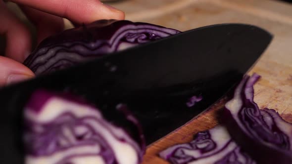 Caucasian hands cuts a red cabbage in small pieces on wooden chopping board. alt
