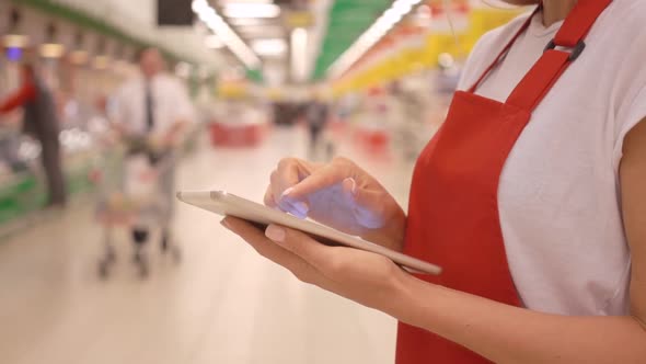 Female supermarket clerk using apps on a digital tablet