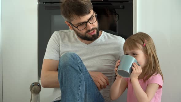 Happy Family Father and Little Daughter Drink Coffee at Home and Laugh alt
