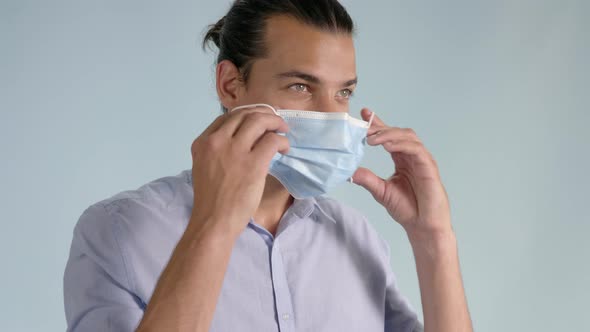 Smiling young man puts on face mask and raises thumbs up turning to camera alt
