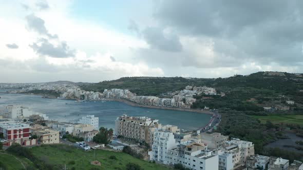 AERIAL: Panoramic Shot of Mellieha Bay with Cars Driving on Roads and Houses in Background alt