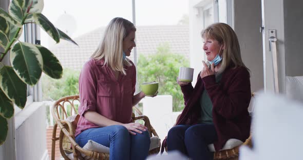 Mother and daughter talking to each other while drinking coffee at home alt