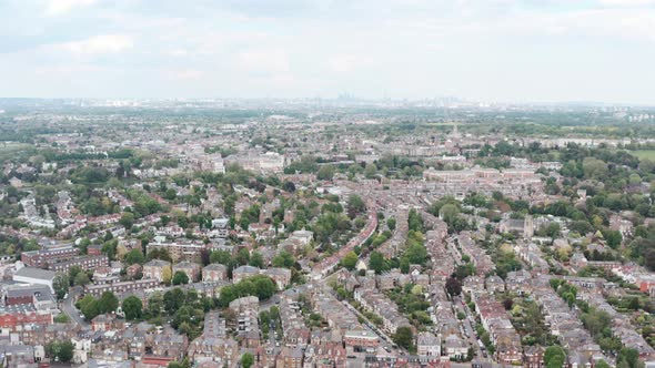 Dolly forward drone shot over dense residential buildings in West London city skyline in background alt