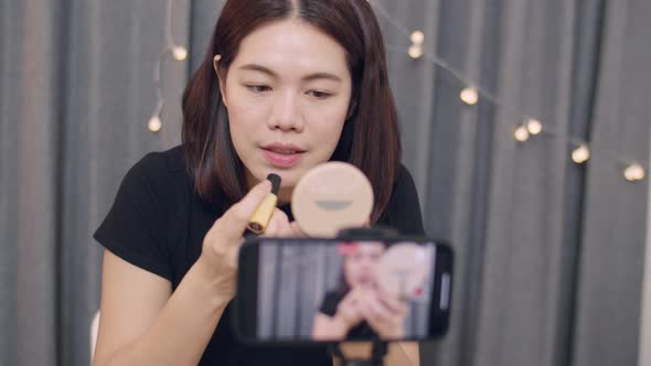 Beautiful Asian woman beauty blogger influencer makeup artist recording on smartphone.