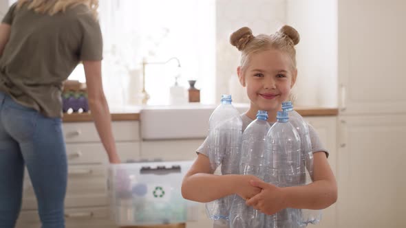 Portrait video of smiling girl holding plastic bottles in kitchen. alt