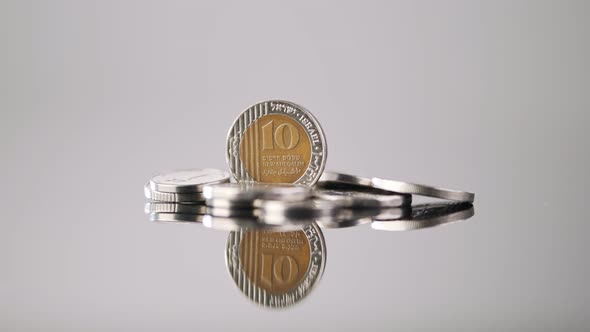 New Israeli Shekels coins rotating on a reflective surface