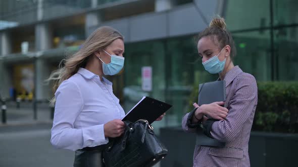 Two young business women wearing medical masks meet on the street to communicate alt