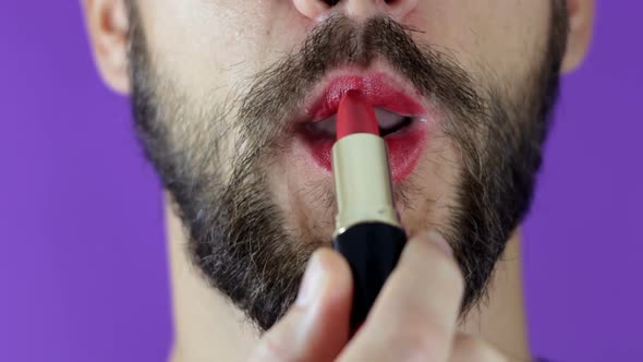 A Young Guy with a Beard Paints His Lips with Red Lipstick