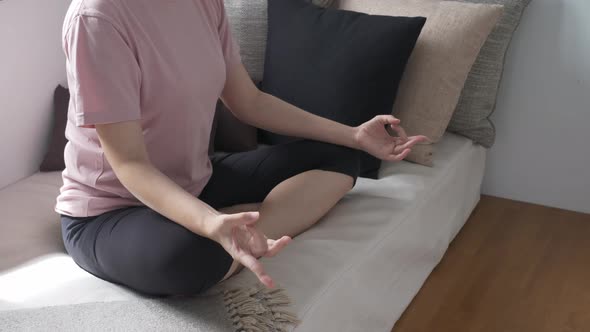 Unrecognizable woman sitting on couch, practicing yoga alt