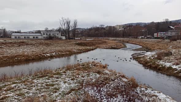Pan shot of 2 rivers joining with ducks beneath overcast against polish mountains alt
