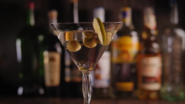 Closeup of a Martini Glass with Olives and Lemon Slowly Rotating on the Bar alt