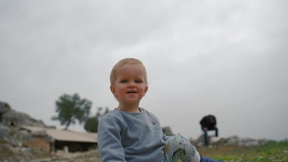 Cute Blond Boy Sits on Ground Playing with Stones at Trip alt