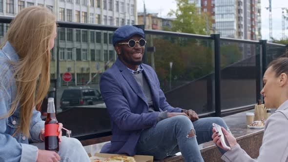 Laughing friends sitting on the street with drinks