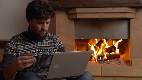 Man Shopping Online Using Laptop at Home Sitting By the Fireplace alt