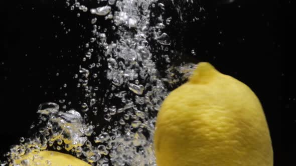Slow Mo Lemons Falling Into Water on Black Background