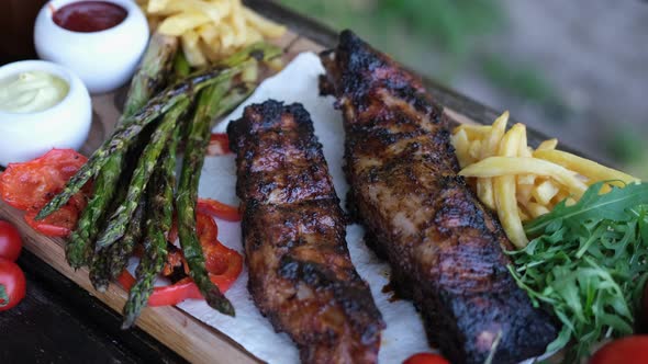 Delicious Beef or Pork Grilled Ribs Served with Aspargus and French Fries on a Wooden Board alt