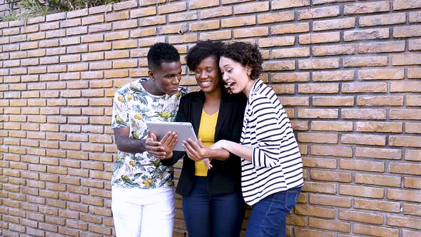 Three young people interact on video call on tablet outdoors alt