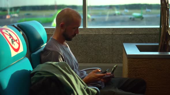 Caucasian Man is Using Device and Waiting for Flight While Sitting at Airport Terminal Spbd alt