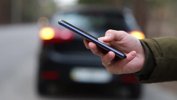 Close-up of a hand using a phone on a background of a car with a flashing alarm alt