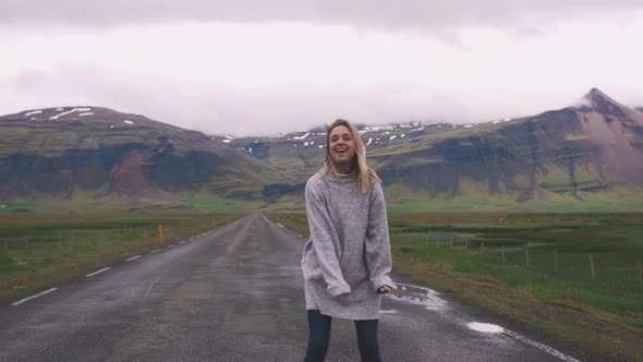 Happy Young Woman Dancing on Asphalt Road in Iceland and Having Some Fun Slow Motion alt