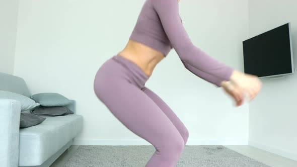 Side view young woman in violet activewear stands on carpet do butt exercises deep squat