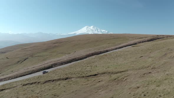 Travel Car Driving in Highland Road on Snowy Mountain Peak Landscape. SUV Car Moving on Highway alt