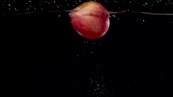 Vibrant red apple being dropped into water in slow motion. alt
