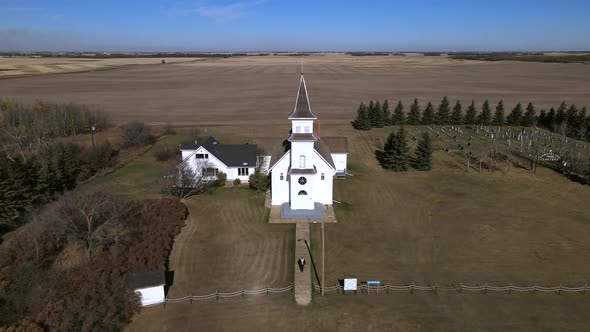 Aerial footage in 4k of rural countryside church in Alberta, Canada. Person walking along path leadi alt