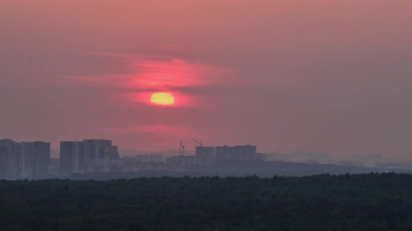 The haze over the houses in the city during the heat, the time-lapse of the setting sunset sun