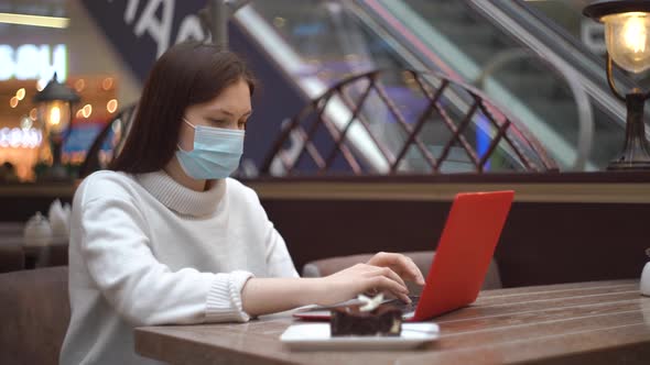 Woman in Protective Mask Working on Laptop in a Shopping Center in a Cafe