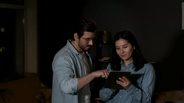 A young woman and man are working in their living room in the dark background alt