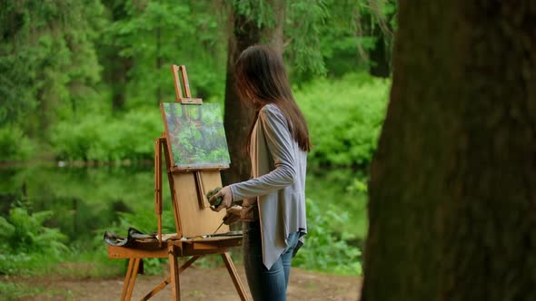 Rear Middle View of a Young Artist Woman Painting a Landscape in a Summer Forest alt