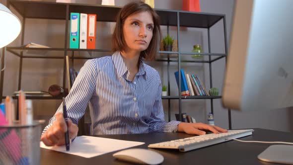 Thinking woman turning pencil at office desk alt