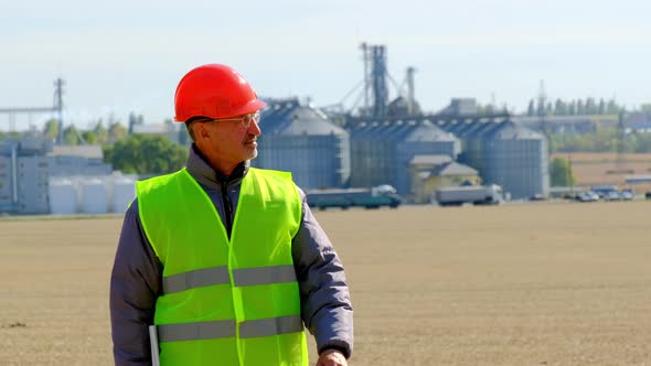 Grain Elevator Engineer Walks Looking at Tablet in Field alt