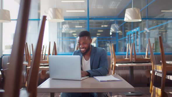 Happy AfricanAmerican Cafe Owner Work on Laptop alt