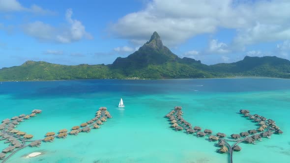 Aerial drone view of a luxury resort, overwater bungalows and sailboat in Bora Bora tropical island alt