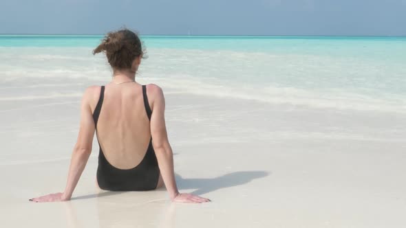 Young Girl Sits on Beach on Shore of Indian Ocean and Looks into Distance.