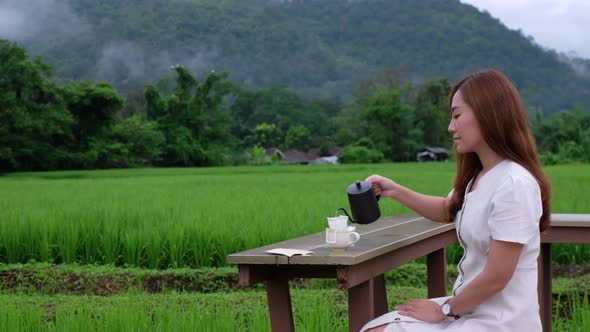 A young woman making drip coffee in the rice field with a beautiful nature view