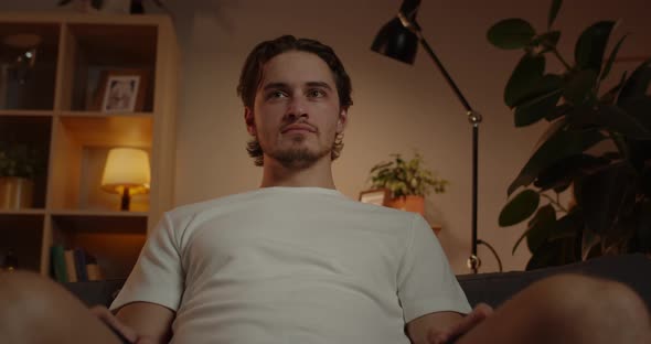 Bottom View of Young Bearded Man Looking Aside While Sitting on Sofa at Home alt