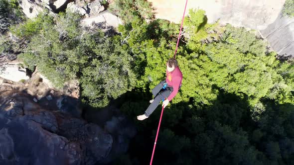 Male highliner sitting on a rope over rocky mountains 4k alt