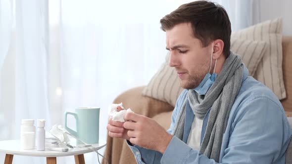 Sick Man Blowing His Nose While Sitting on Sofa at Home alt