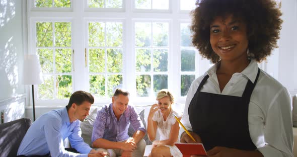 Portrait of smiling waitress with notepad while friends interacting in background alt