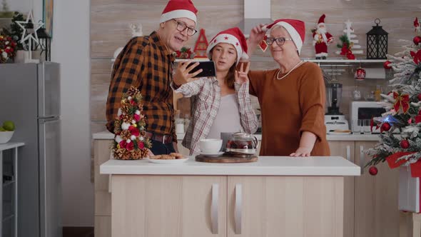 Family Taking Selfie Using Smartphone Enjoying Winter Holiday in Xmas Decorated Kitchen alt