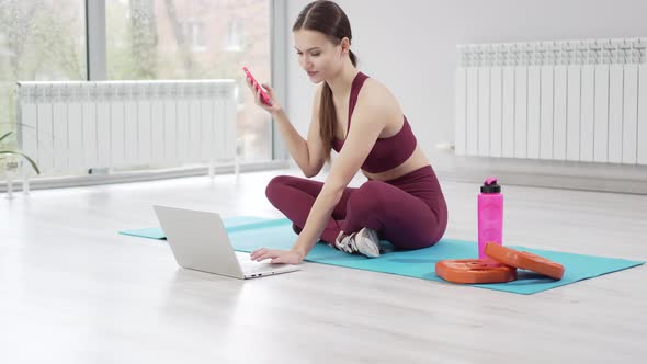 a Young Woman with Laptop Sends a Message to Students for an Online Workout alt