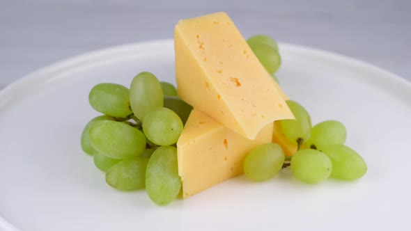 Rotating Slices of Cheese with Grapes on a White Plate or Background Closeup Snack Concept