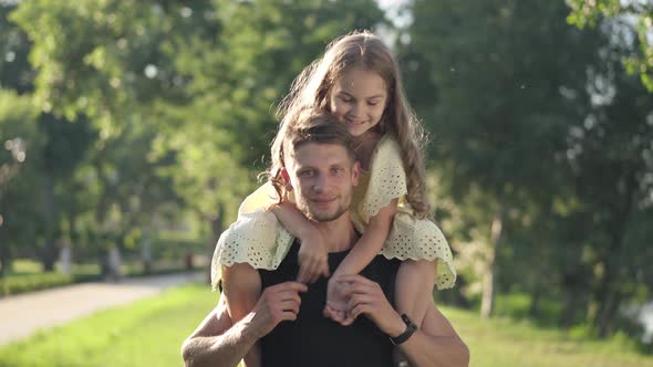 Positive Man Looking at Camera Smiling with Pretty Girl on Shoulders alt