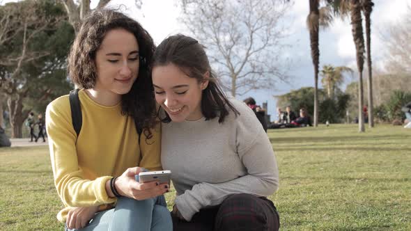 Two beautiful girls using smartphone at park and sharing on social media