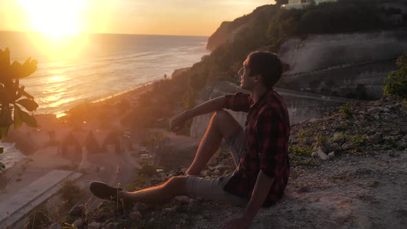 Man Traveler Sits on the Rock Enjoying the View of Sunset Sea
