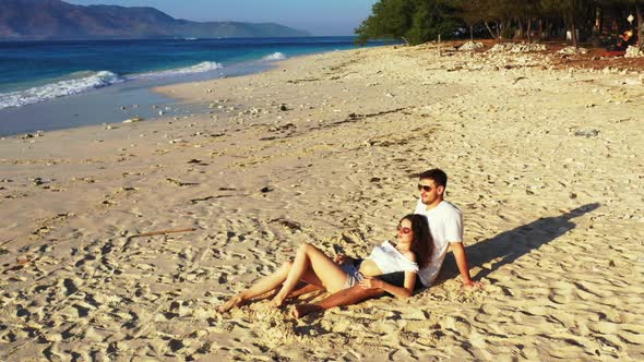 Two lovers happy together on relaxing resort beach voyage by blue lagoon with white sandy background alt